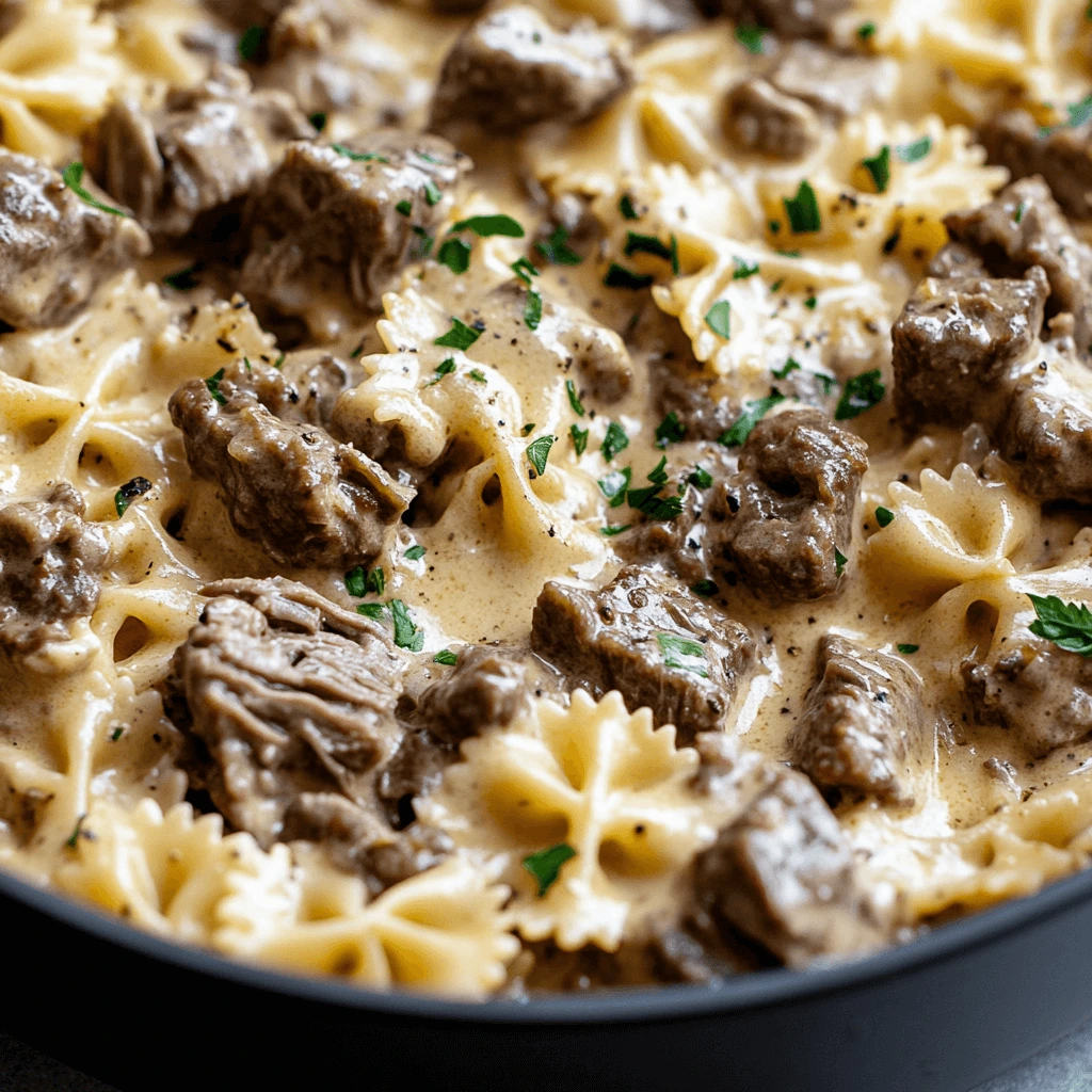 A bowl of Creamy Beef and Bowtie Pasta topped with Parmesan cheese, fresh spinach, and roasted cherry tomatoes.