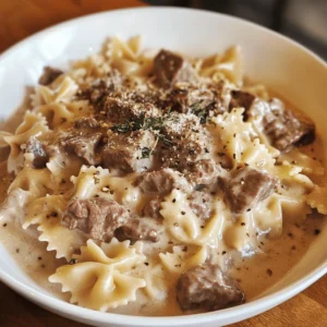 A plate of Creamy Beef and Bowtie Pasta garnished with Parmesan cheese, fresh spinach, and roasted cherry tomatoes.